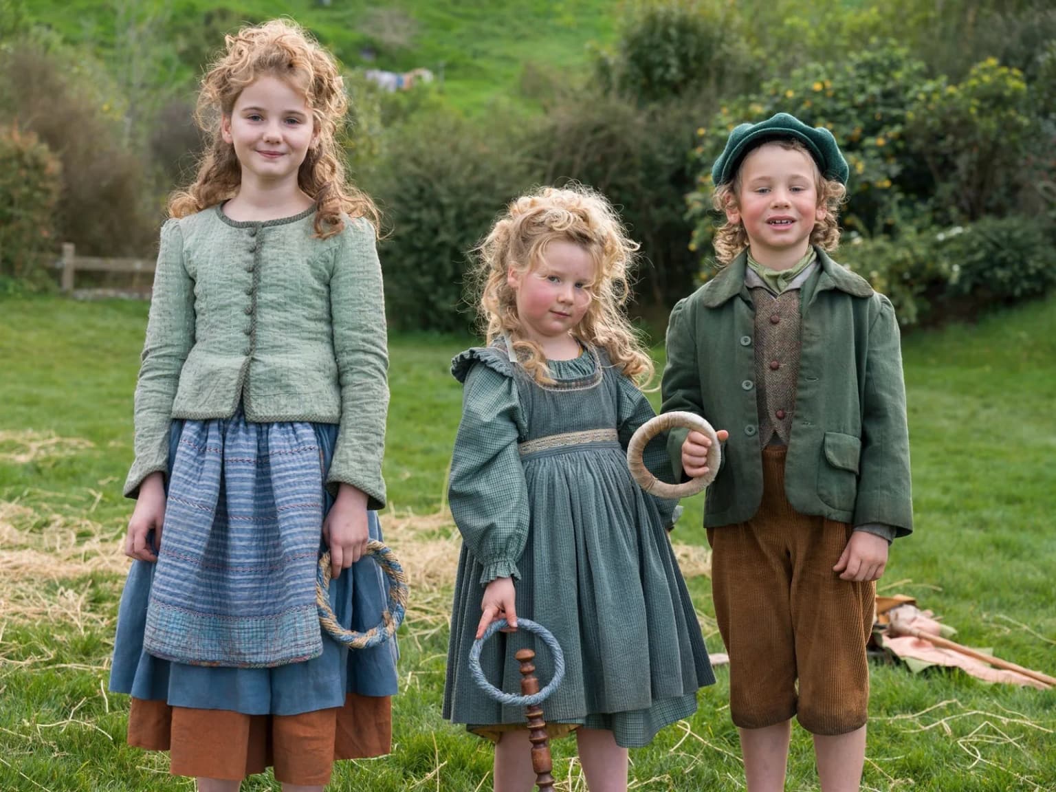 Trois jeunes Hobbits jouent au jeu du cerceau et du bâton sur l'herbe