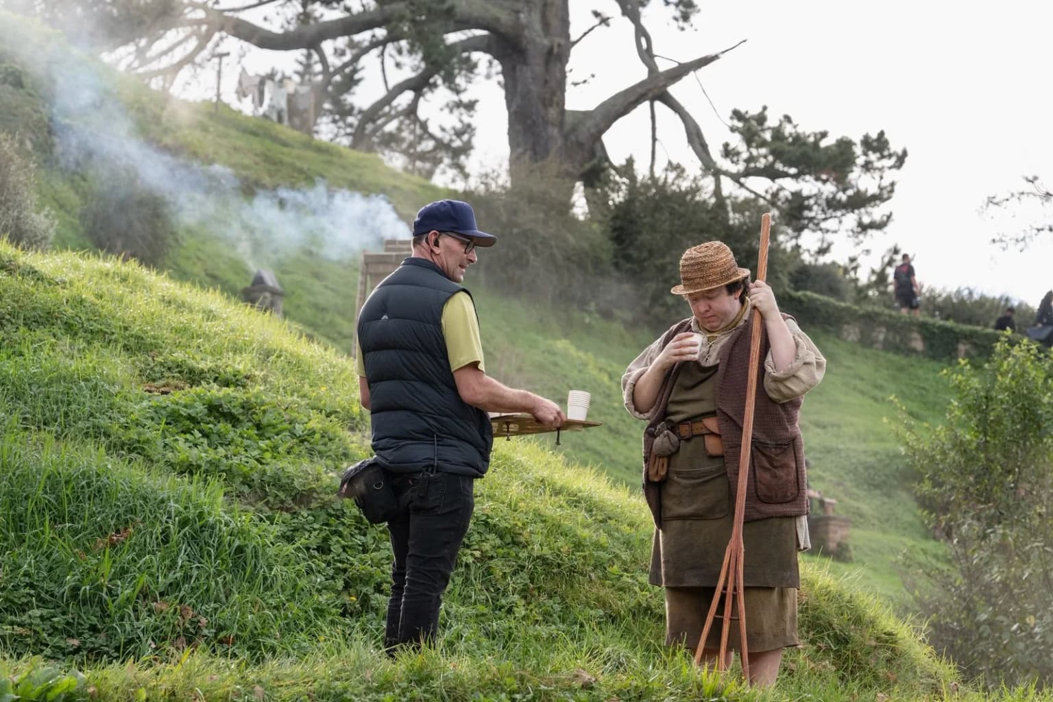 Un membre de l'équipe sert un café à un figurant hobbit en pause entre deux prises