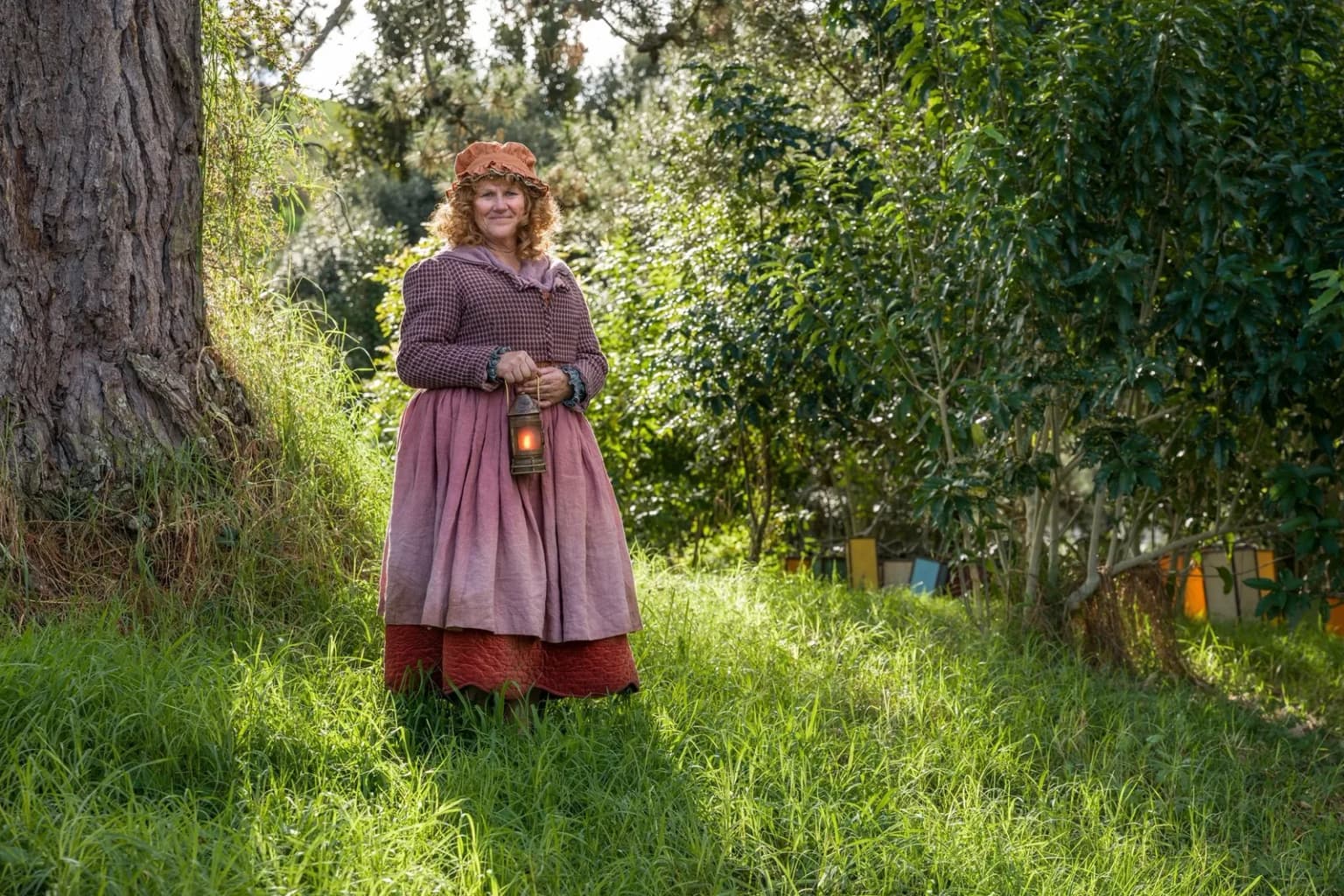 Une Hobbit en robe rose tient une lanterne allumée dans un sous-bois