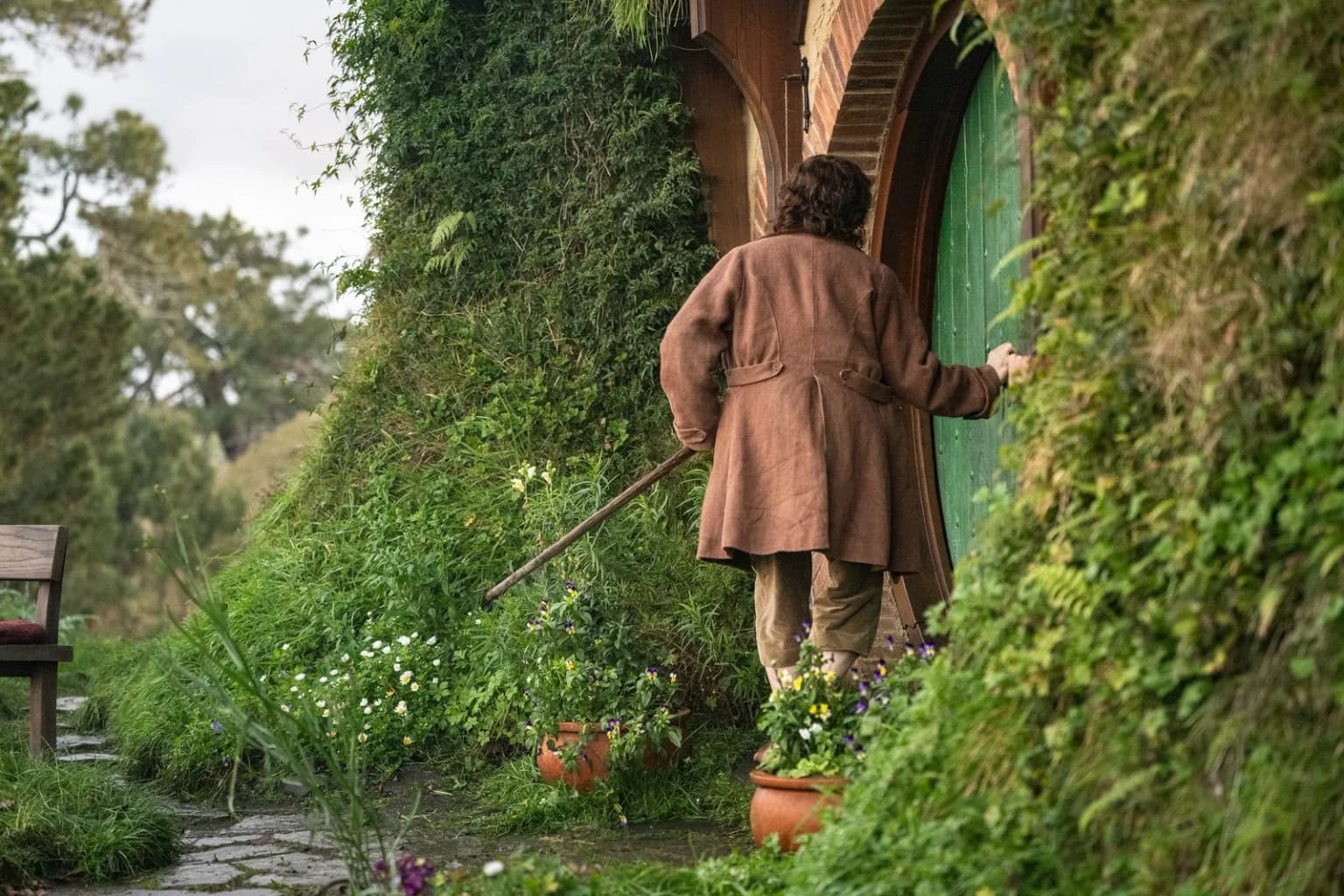Un Hobbit franchit le seuil de sa porte ronde à Hobbiton